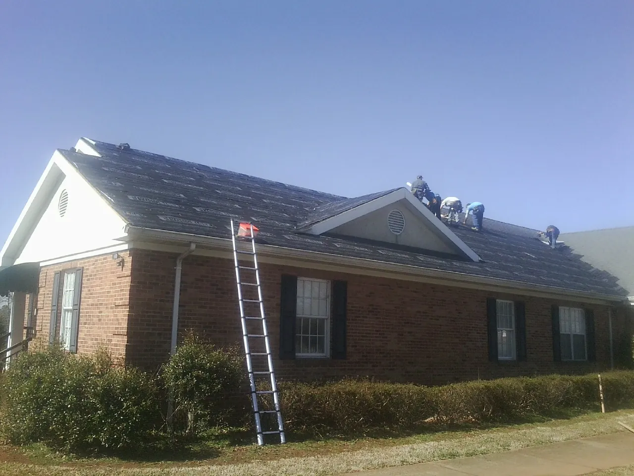 Crew tearing shingles off a brick ranch roof with a ladder set — Emergency Roof Repair work by our crew in East Brunswick
