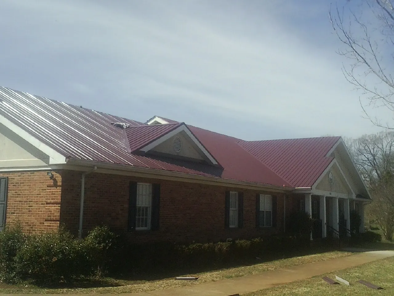 Red metal roof with gabled entries on a long brick building, from a Hail Damage Roof Repair job in East Brunswick