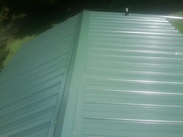 New green metal panels meeting at the ridge of a roof — Flat Roof Repair work by our crew in East Brunswick
