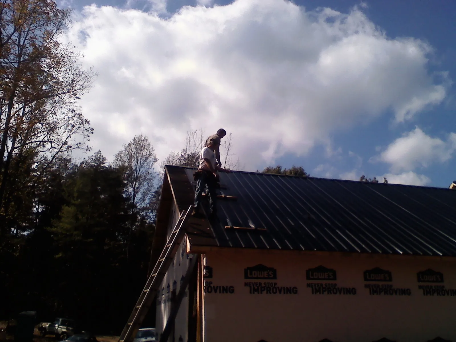 Roofer fastening dark metal panels high against a cloudy sky, from a Roof Inspection job in East Brunswick
