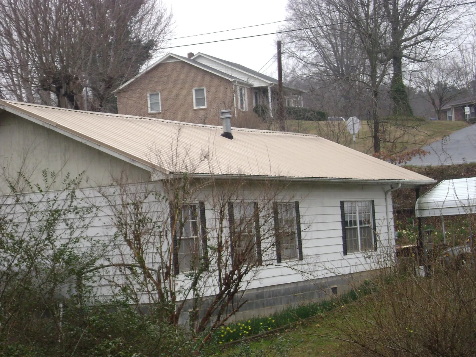 Tan metal roof on a white sided house set into a hillside — Commercial Roofing by Roofing Brothers in East Brunswick